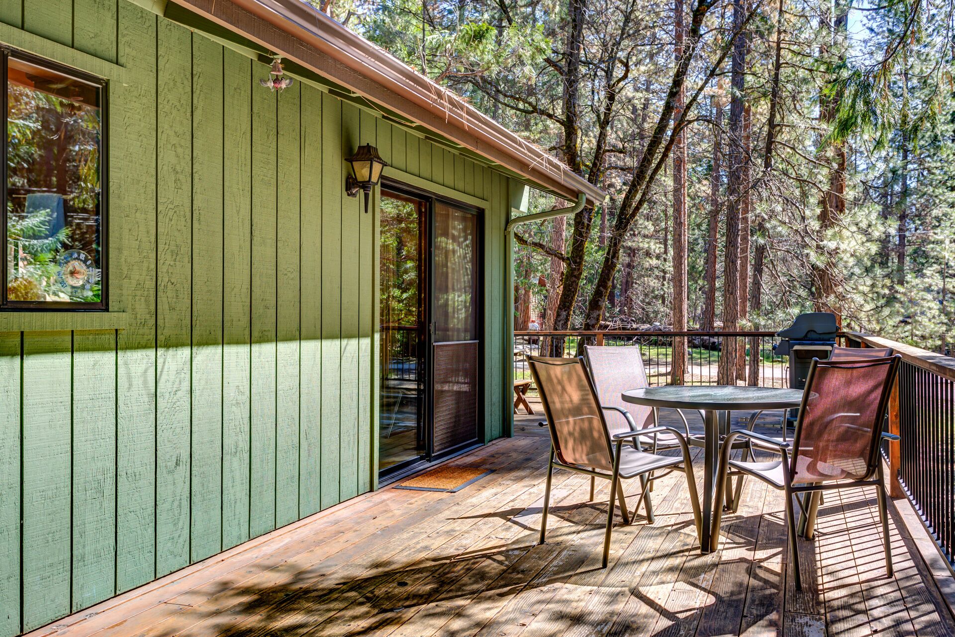Una terraza de madera con una mesa y sillas, rodeada de un bosque.