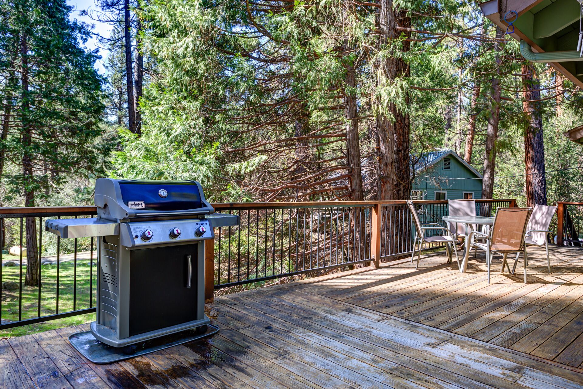 Una parrilla para barbacoa en una terraza de madera con vistas a un bosque y una casa al fondo.