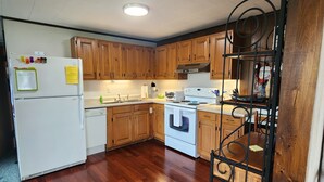 A kitchen with wooden cabinets, a white refrigerator, a stove, and a sink. - Located In The Heart Of Meredith Bay (Meredith)