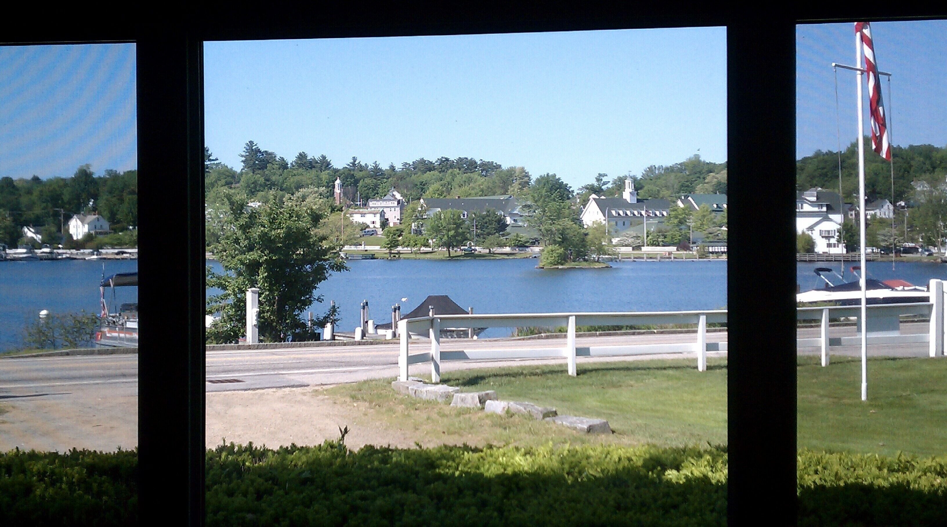 A lakeside view with a dock, a flagpole, and houses in the background.