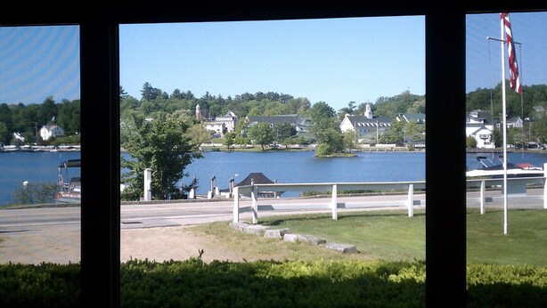 A lakeside view with a dock, a flagpole, and houses in the background. - Located In The Heart Of Meredith Bay (Meredith)