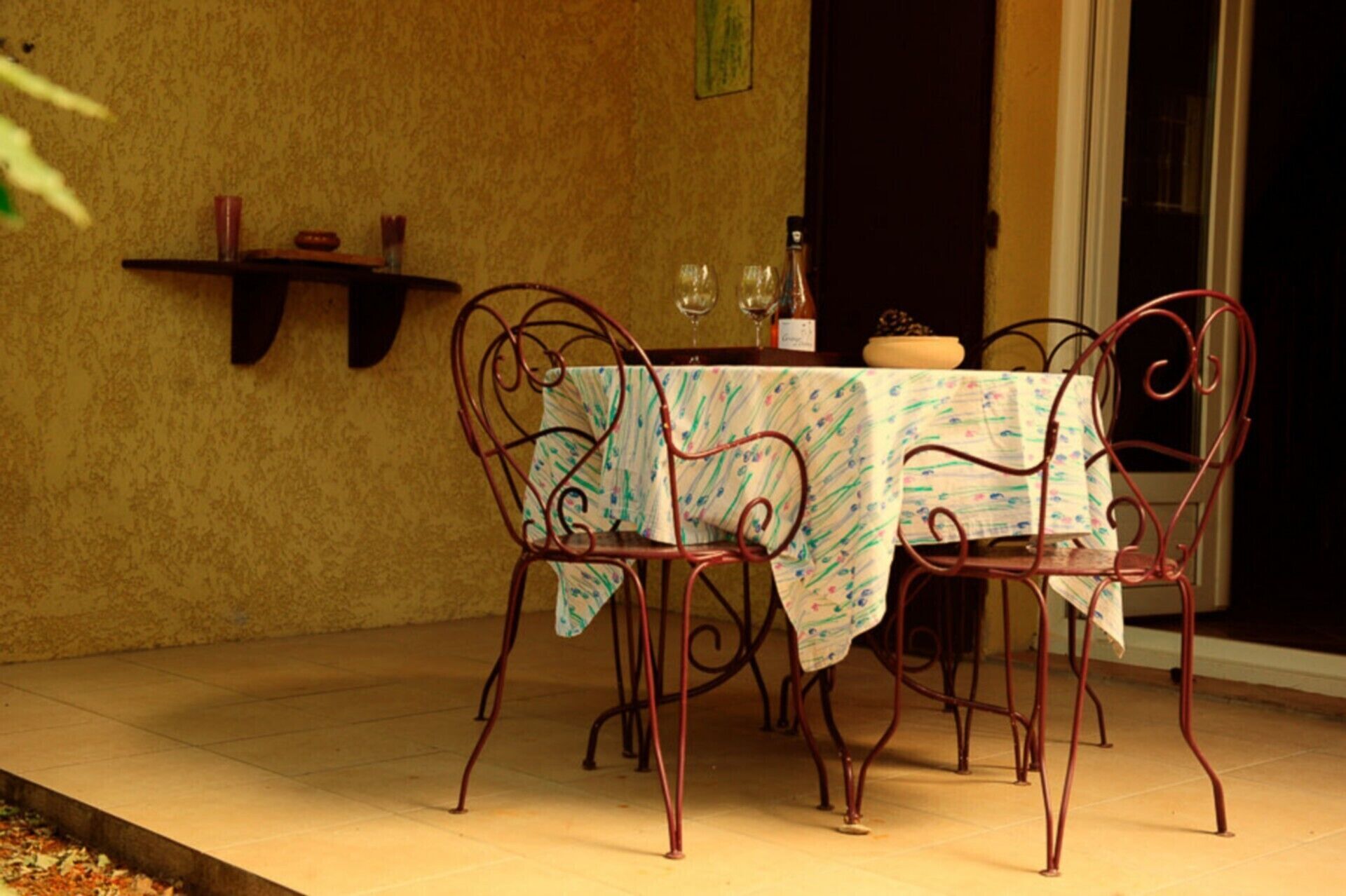 An outdoor patio with a table set for two, surrounded by metal chairs, against a textured wall.