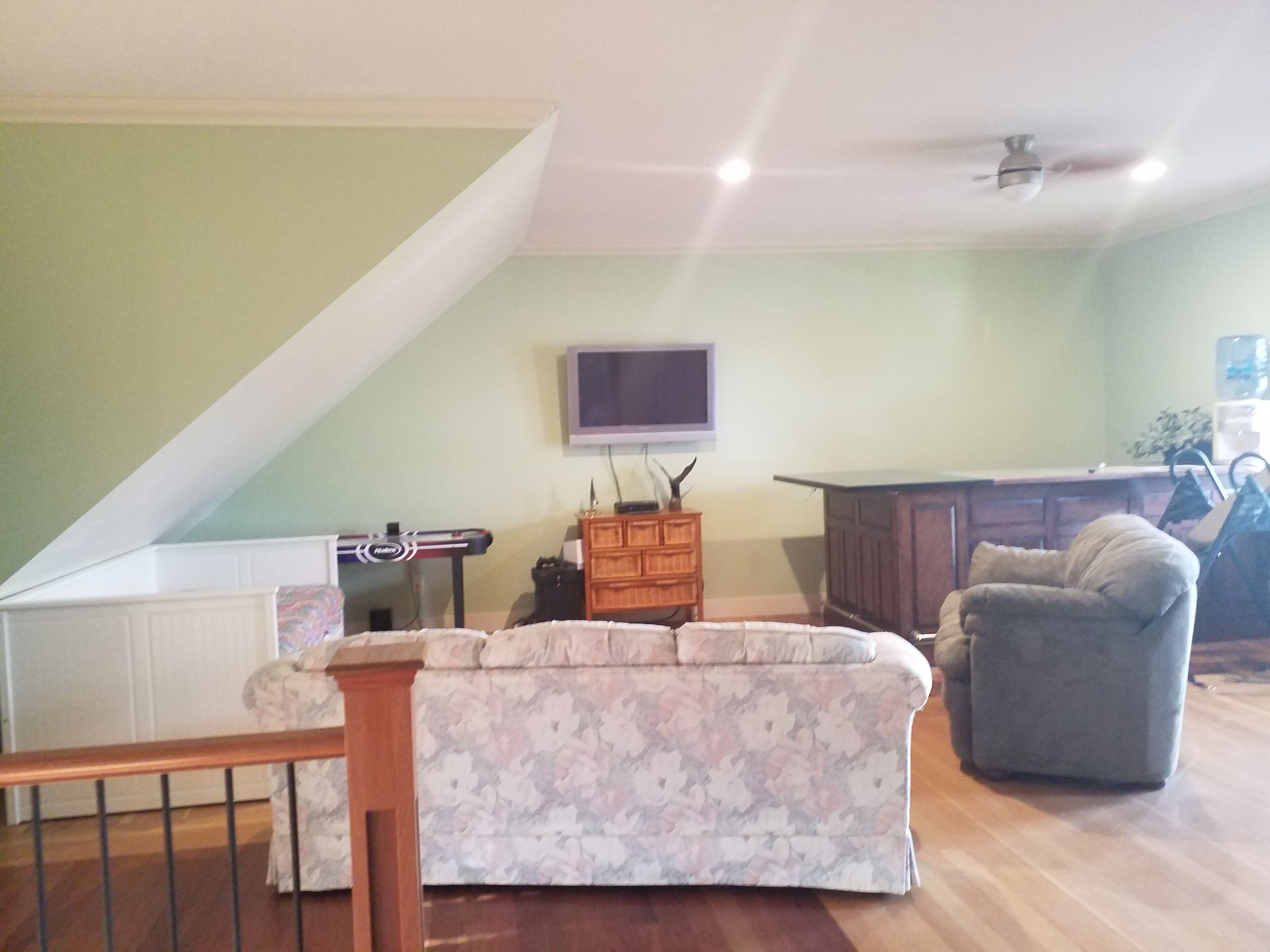 A living room with a high ceiling, a television mounted on the wall, a wooden cabinet, a gray armchair, and a patterned sofa.