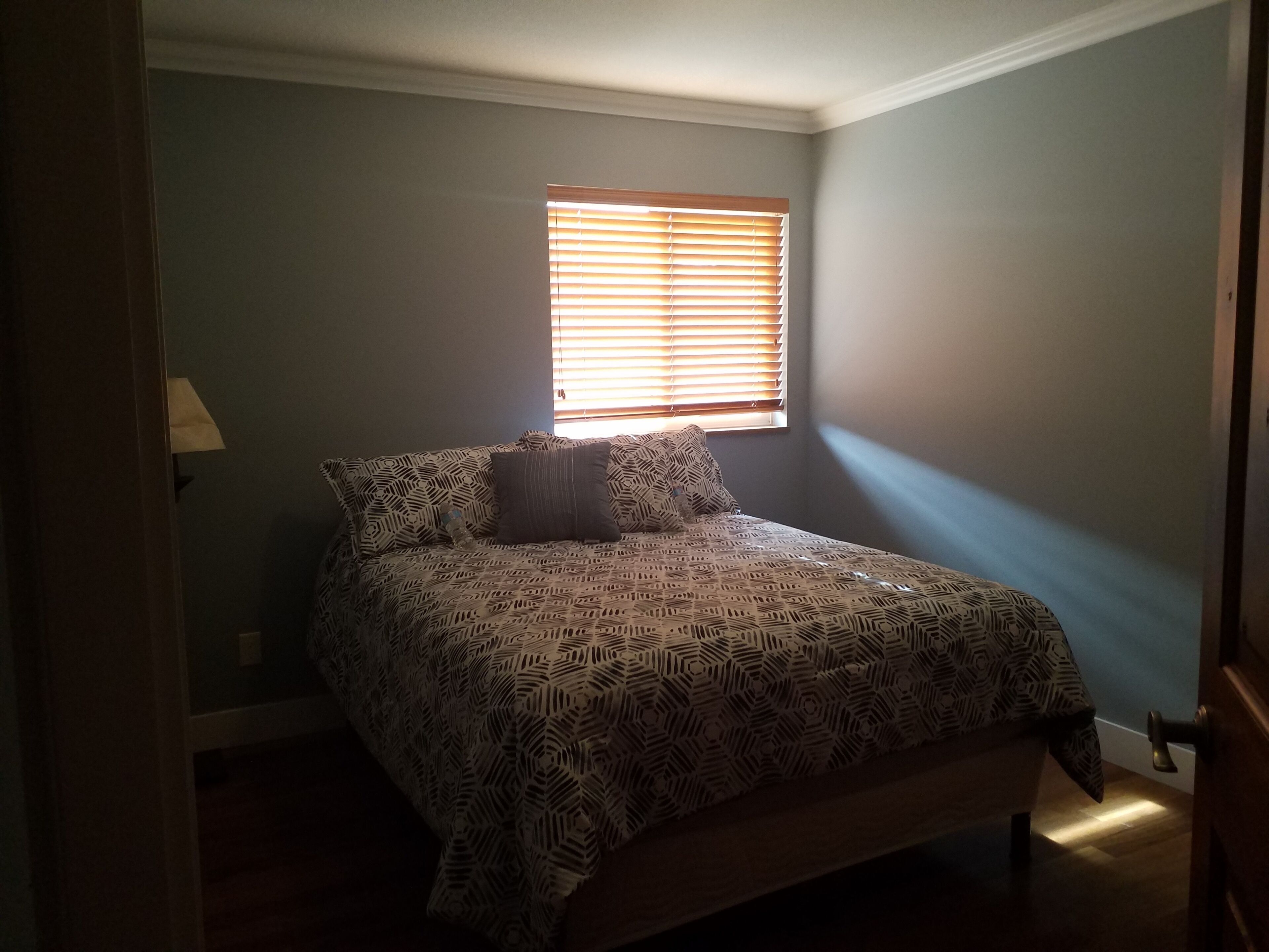 Ein Schlafzimmer mit einem Bett, einem Fenster mit Jalousien und einer Tür.