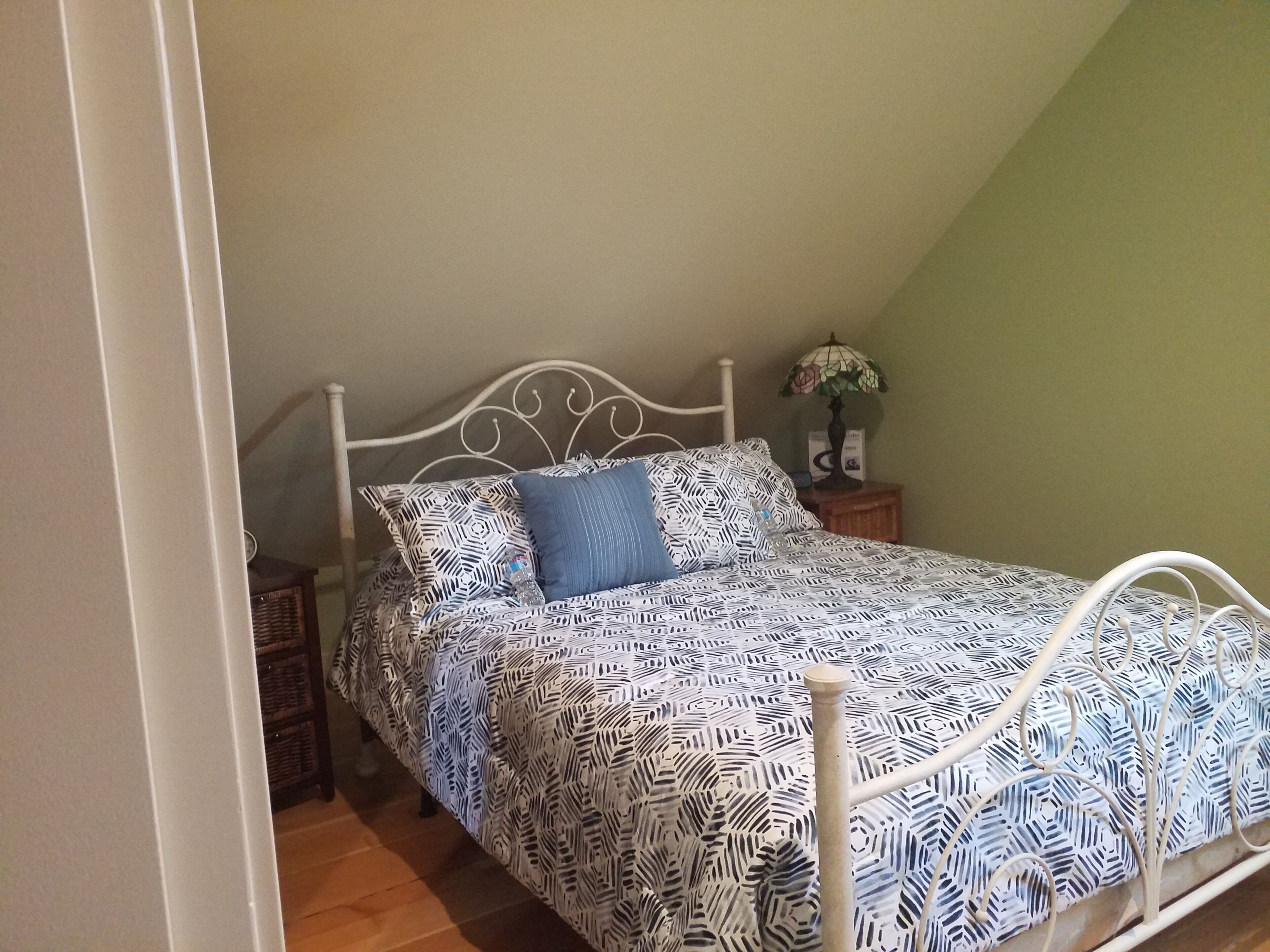 Un lit simple avec une couvre-lit à motifs, un oreiller bleu et une table de chevet sur laquelle se trouvent une lampe et un petit cadre photo.