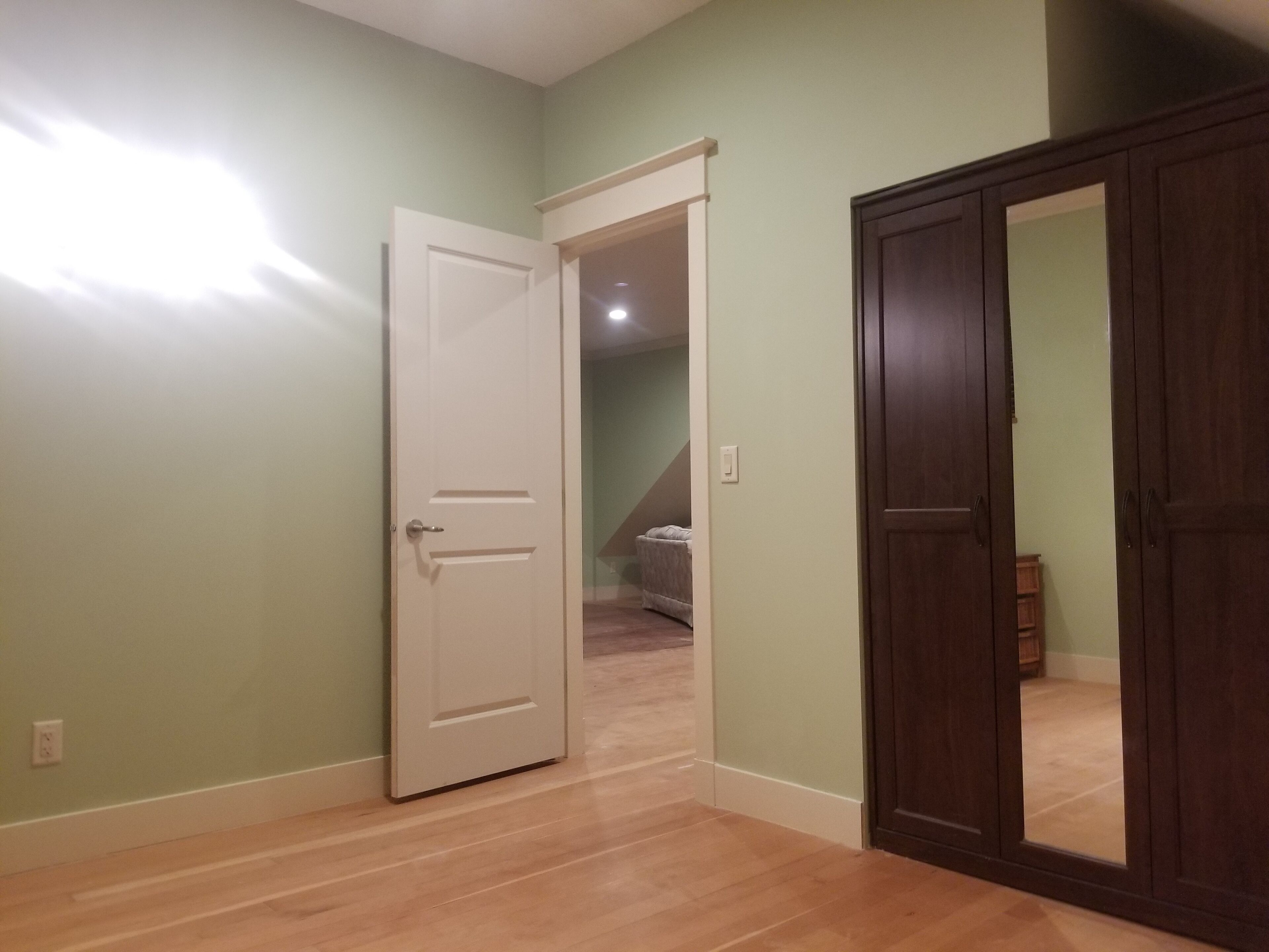 Une pièce avec un plancher en bois, une porte blanche et une porte en bois foncé.