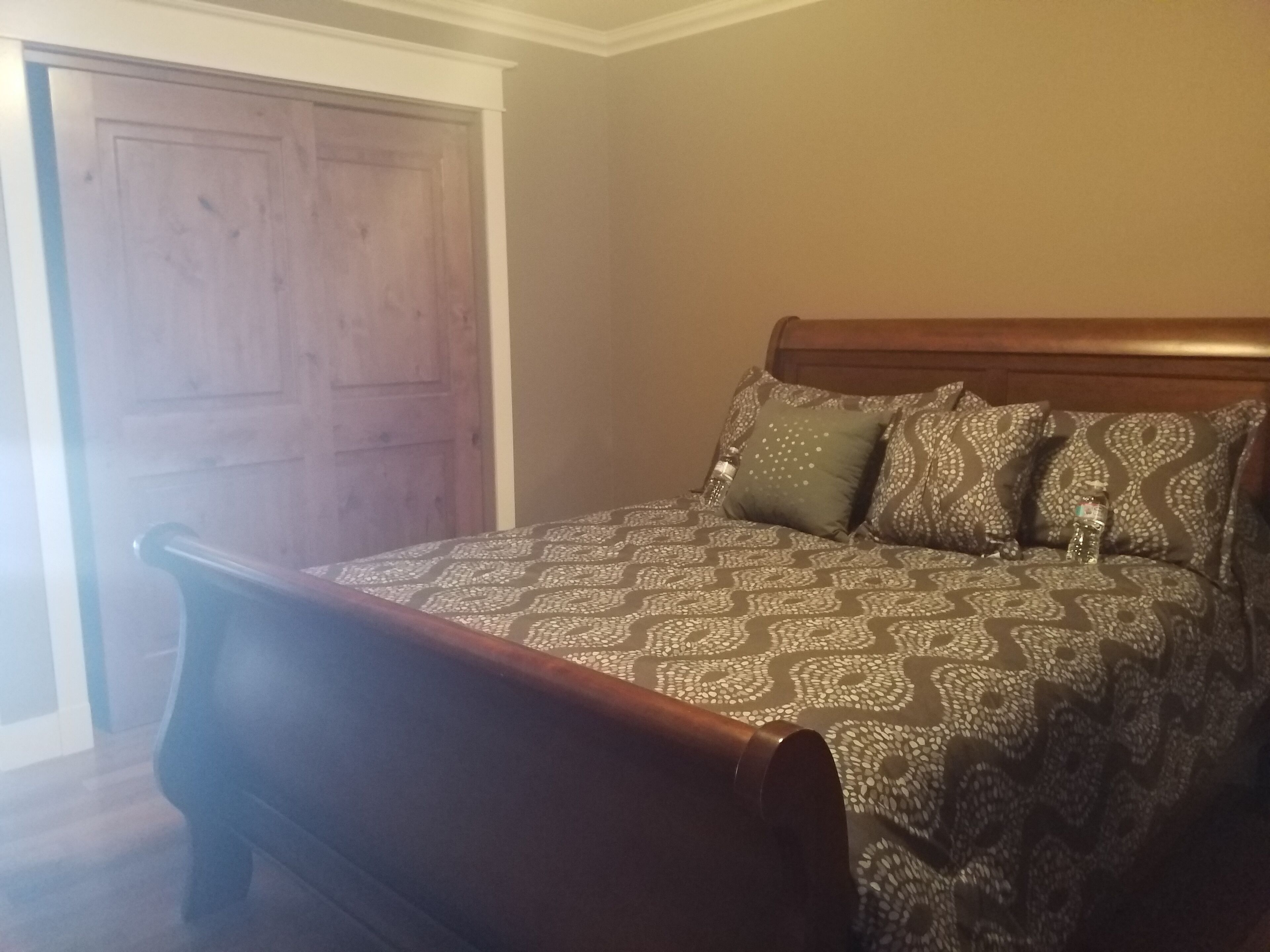 A bedroom with a wooden bed frame, patterned bedding, and a wooden door.