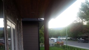 Puuinen terassi, jossa on ulkotilaa istumiseen, kivimuuri sekä näkymä tielle ja puille.