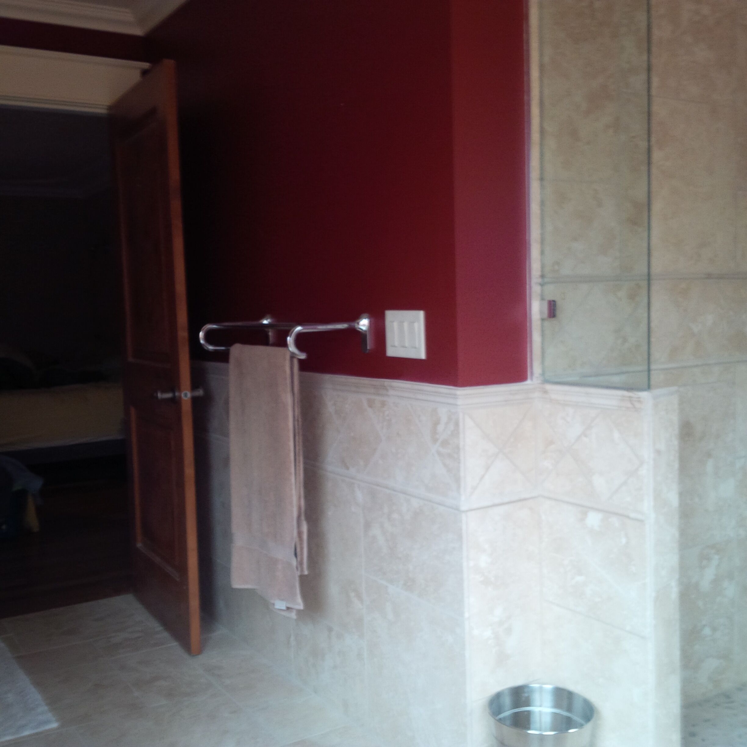 Ein Badezimmer mit roter Wand, einem Handtuchhalter, einem Metallwaschbecken und einer Tür.