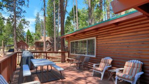 A wooden deck with a table and chairs, surrounded by tall trees.