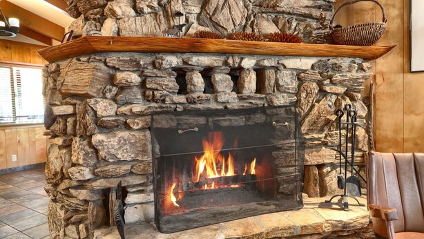 A stone fireplace with a fire, a wooden shelf above it, and a chair to the right.