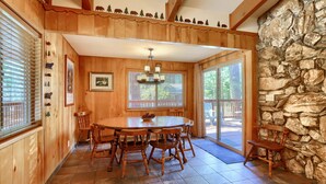 A wooden dining area with a large table and chairs, a stone wall, and a view of the outdoors.