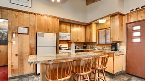 A kitchen with wooden cabinets, a refrigerator, a microwave, a stove, and a sink. There are two wooden bar stools at the island.