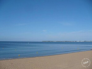 A beach with a clear sky, calm sea, and a distant pier.