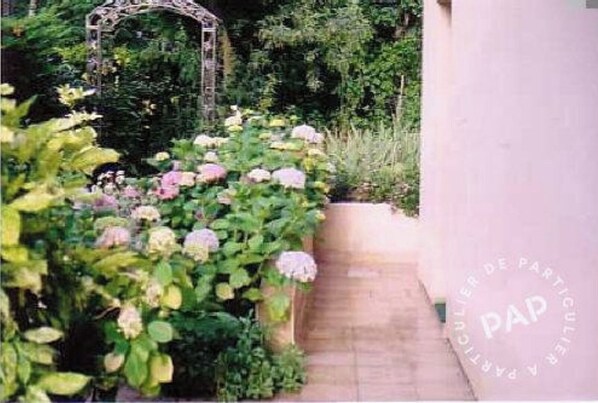 A garden pathway with a metal archway, surrounded by lush greenery and flowering plants.