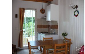 A kitchen with a sink, stove, and cabinets, a dining table with chairs, and a window with curtains.
