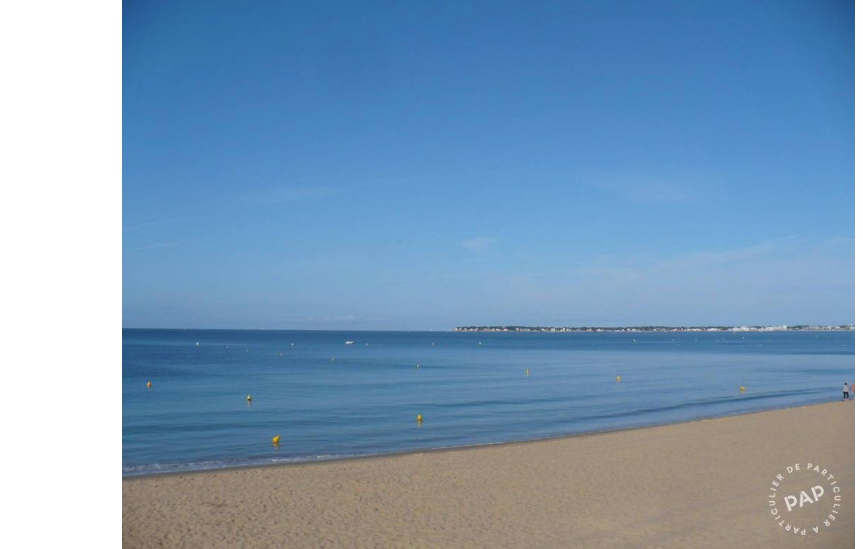 A beach with a clear sky, calm sea, and a distant pier.