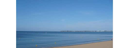Una playa con cielo despejado, mar tranquilo y un muelle a lo lejos.