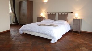 Een slaapkamer met een groot bed, een houten garderobe, twee nachtkastjes met lampen en een betegelde vloer.