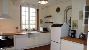 Een keuken met witte kastjes, een spoelbak, een magnetron, een koelkast en een raam met planten.