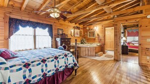 A wooden cabin bedroom with a bed, a vanity, a bathtub, and a door leading to another room. - Cabin on the Hill family friendly (Russell Springs)