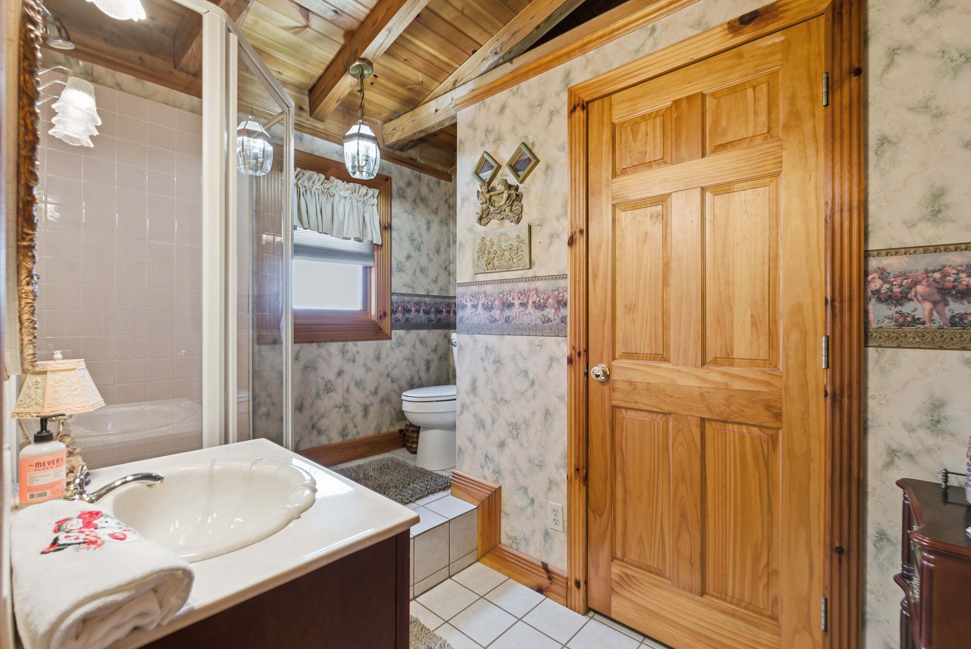 A bathroom with a wooden door, a sink, a mirror, and a shower.