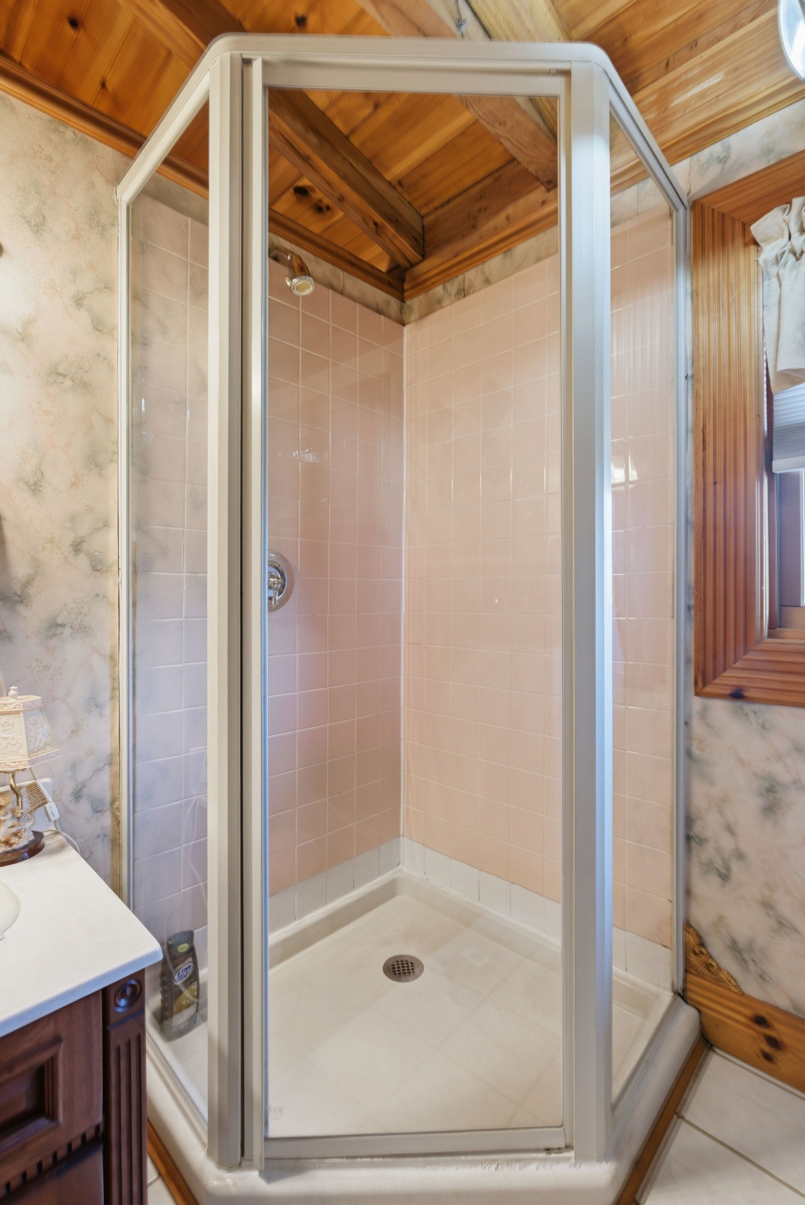 Un cerramiento de ducha con puerta de cristal, vigas de madera en el techo y suelo de baldosas.