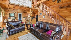 A wooden cabin interior with a leather sofa, a chandelier, a staircase, and a dining area. - Cabin on the Hill family friendly (Russell Springs)