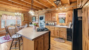 A wooden cabin interior with a kitchen island, wooden cabinets, and a dining area. - Cabin on the Hill family friendly (Russell Springs)