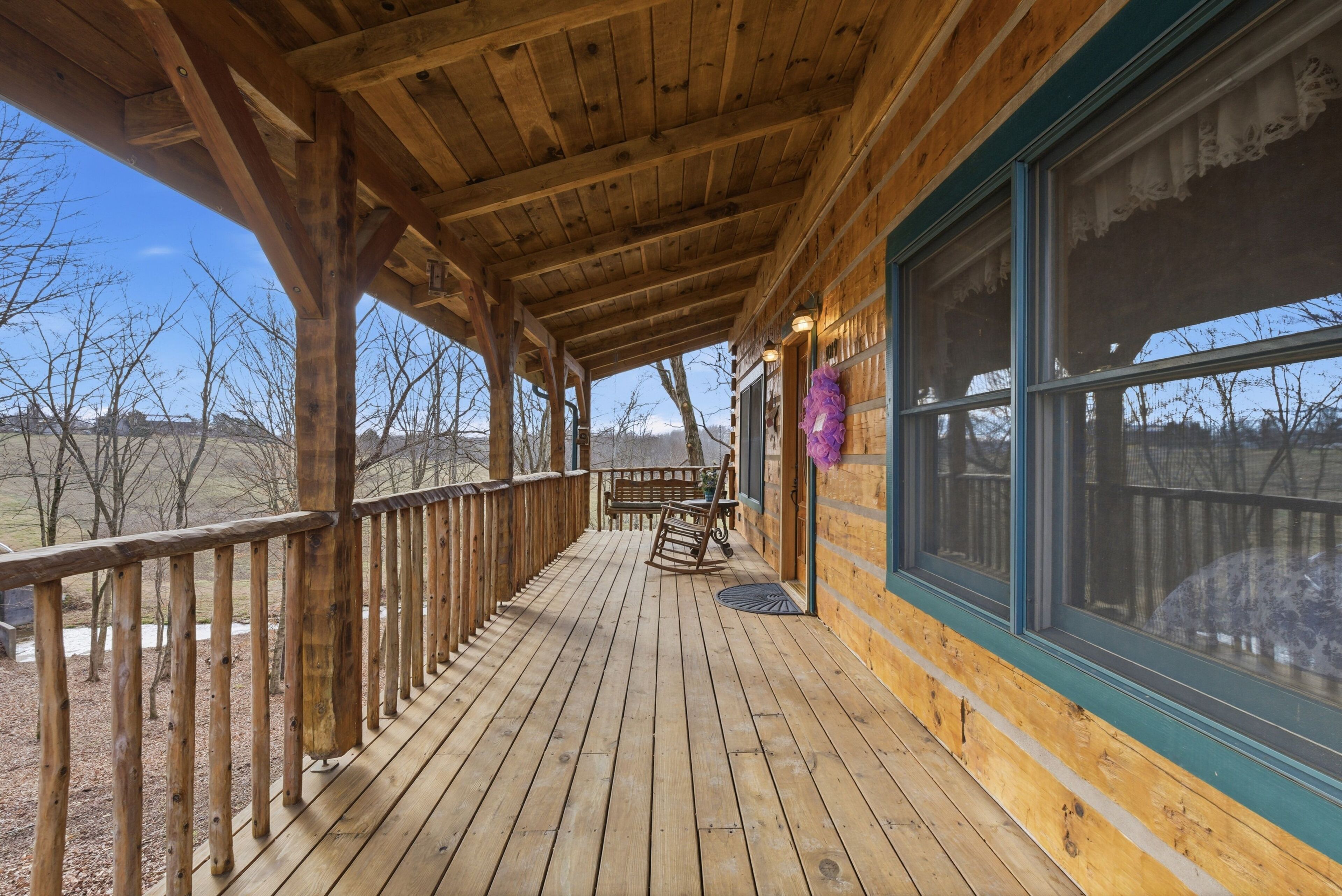 A wooden deck with a railing, a rocking chair, and a window with a view of the outdoors.