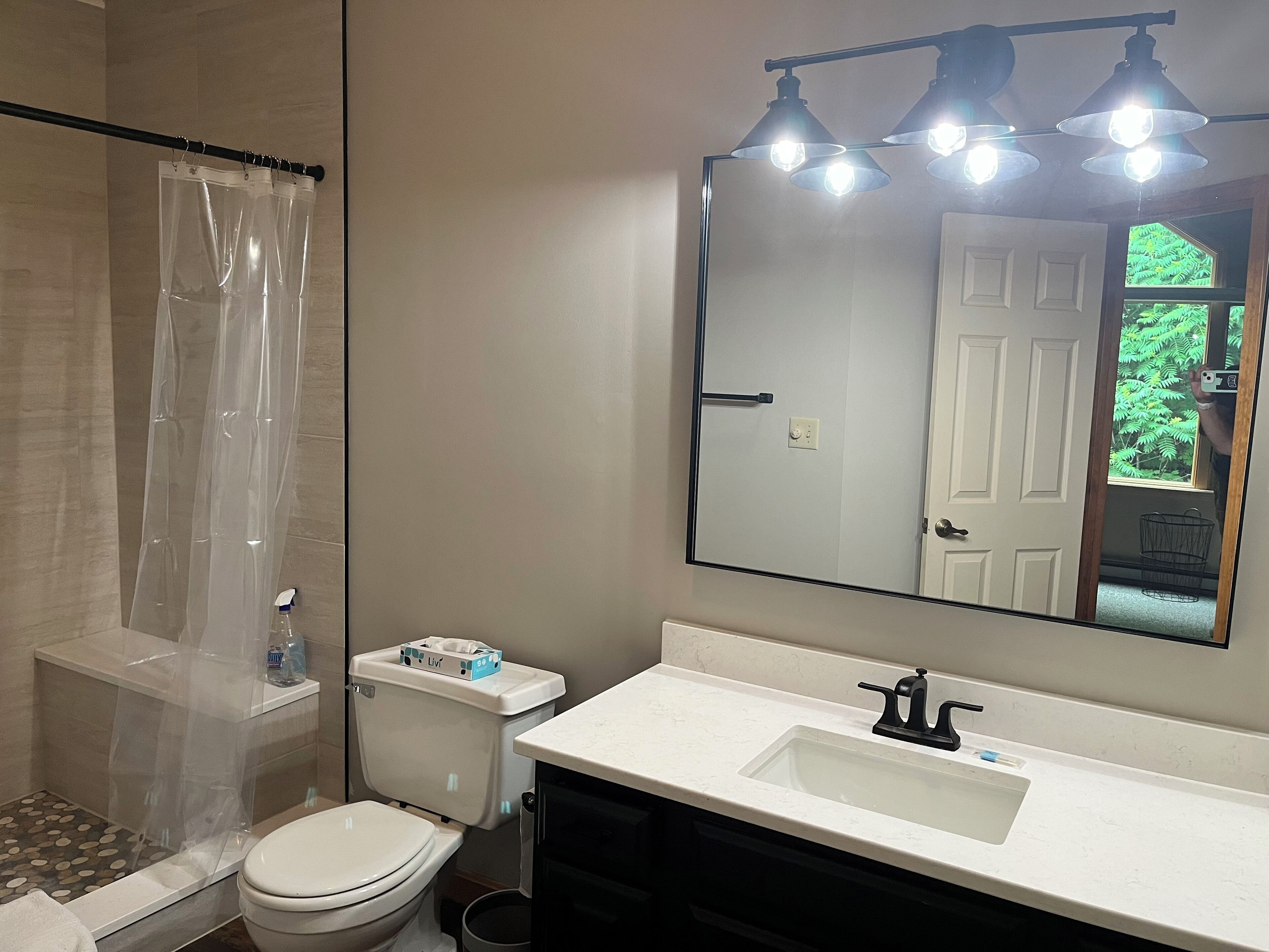 A bathroom with a shower, toilet, sink, and a large mirror.