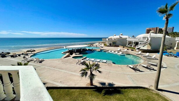 Een resort met een groot zwembad, ligbedden en uitzicht op de oceaan.