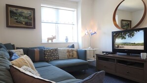 A living room with a sofa, a television, and a window with a view of a dog.