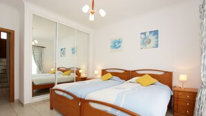 Un dormitorio con cama doble, cabecera de madera, mesitas de noche con lámparas, puerta de cristal corredera y dos cuadros de flores colgados en la pared.