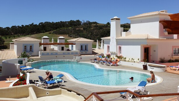 Un área de piscina con sillas de descanso, una piscina y edificios de estilo arquitectónico mediterráneo.