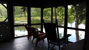 Zona relax esterna coperta, con sedie e tavolo in legno, affacciata su un lago tranquillo e una vegetazione rigogliosa.