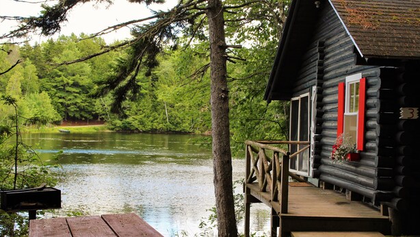 Una baita con veranda in legno che si affaccia su un lago, circondata da alberi.