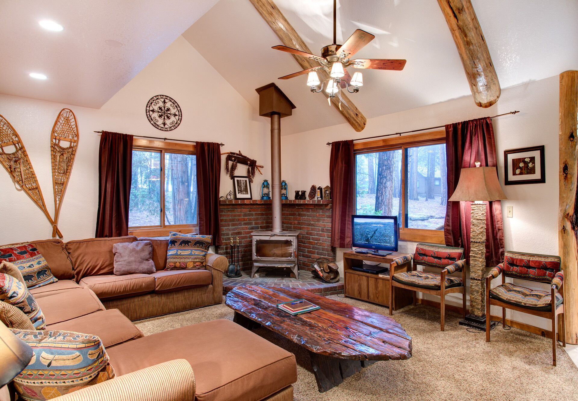 Una sala de estar acogedora con chimenea, muebles de madera y grandes ventanales con vistas a un bosque.
