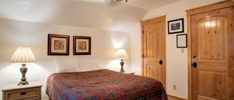 A bedroom with a bed, two bedside lamps, a ceiling fan, and wooden doors.