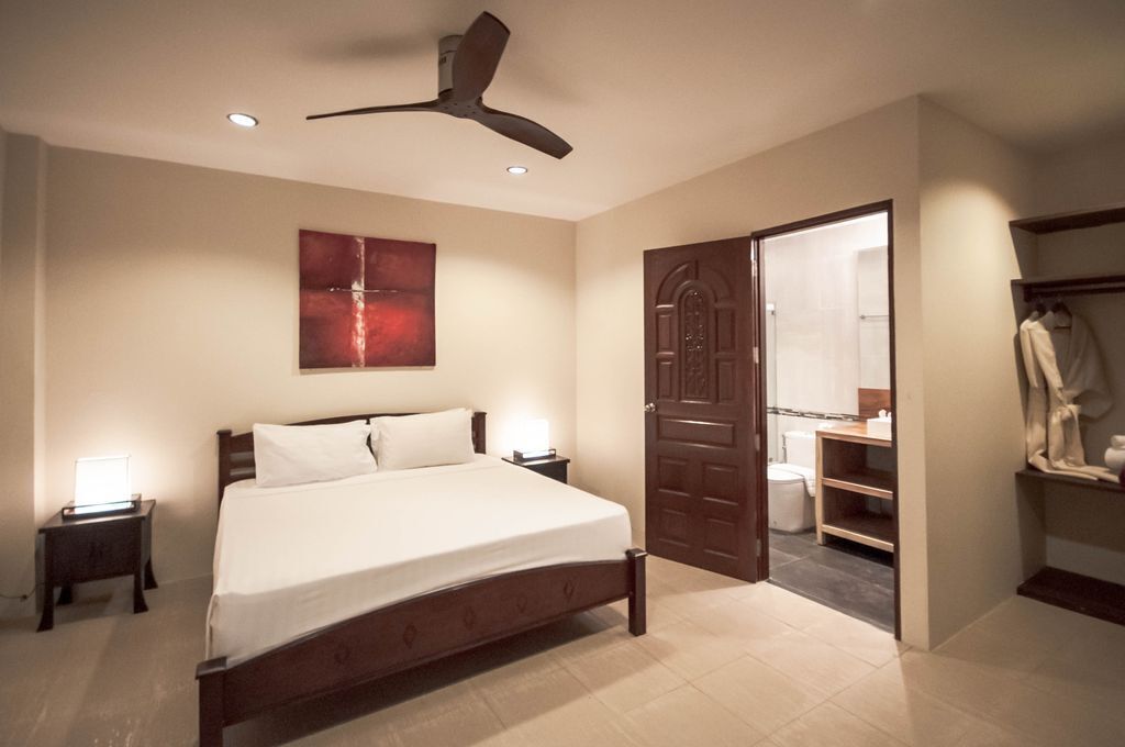 A bedroom with a bed, bedside lamps, a ceiling fan, a door leading to a bathroom, and a closet.