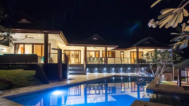 Ein Haus bei Nacht mit Swimmingpool, überdachter Terrasse und gut beleuchtetem Innenraum.