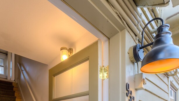 Un escalier menant à une porte dotée d’un panneau en verre dépoli, une boîte aux lettres et un luminaire fixé au mur.