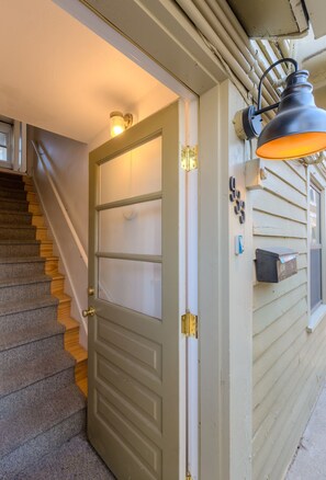 Un escalier menant à une porte dotée d’un panneau en verre dépoli, une boîte aux lettres et un luminaire fixé au mur.