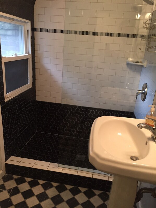 Une salle de bain avec un carrelage noir et blanc à motifs de damier, un lavabo blanc et un espace douche avec des carreaux hexagonaux noirs.