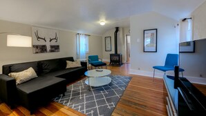 Un salon moderne avec un canapé noir, une table basse en verre et un fauteuil bleu. On y trouve une cheminée et un téléviseur posé sur un meuble.