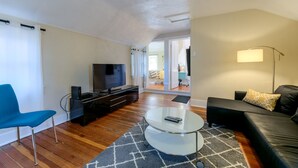 Un salon moderne avec un téléviseur à écran plat, un fauteuil bleu, une table basse en verre et un canapé noir.