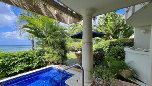 Een zwembad met uitzicht op zee, omringd door weelderige begroeiing en een pergola.