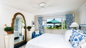 Een slaapkamer met een groot bed, een plafondventilator, een raam met gordijnen en uitzicht op de omgeving.