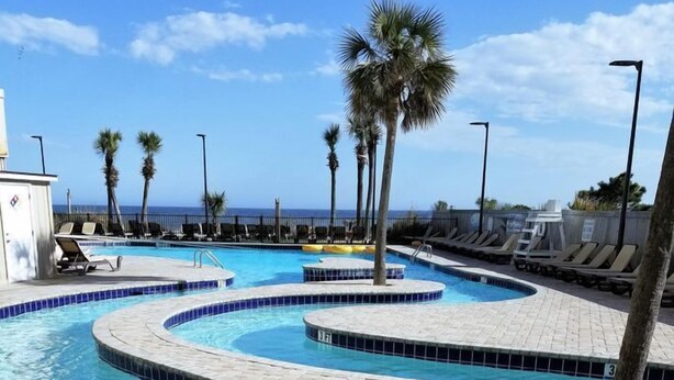 A swimming pool with multiple lanes, palm trees, and lounge chairs. - Caribbean Paradise-Romantic Oceanfront Canopy King Suite with Breathtaking Views (Myrtle Beach)