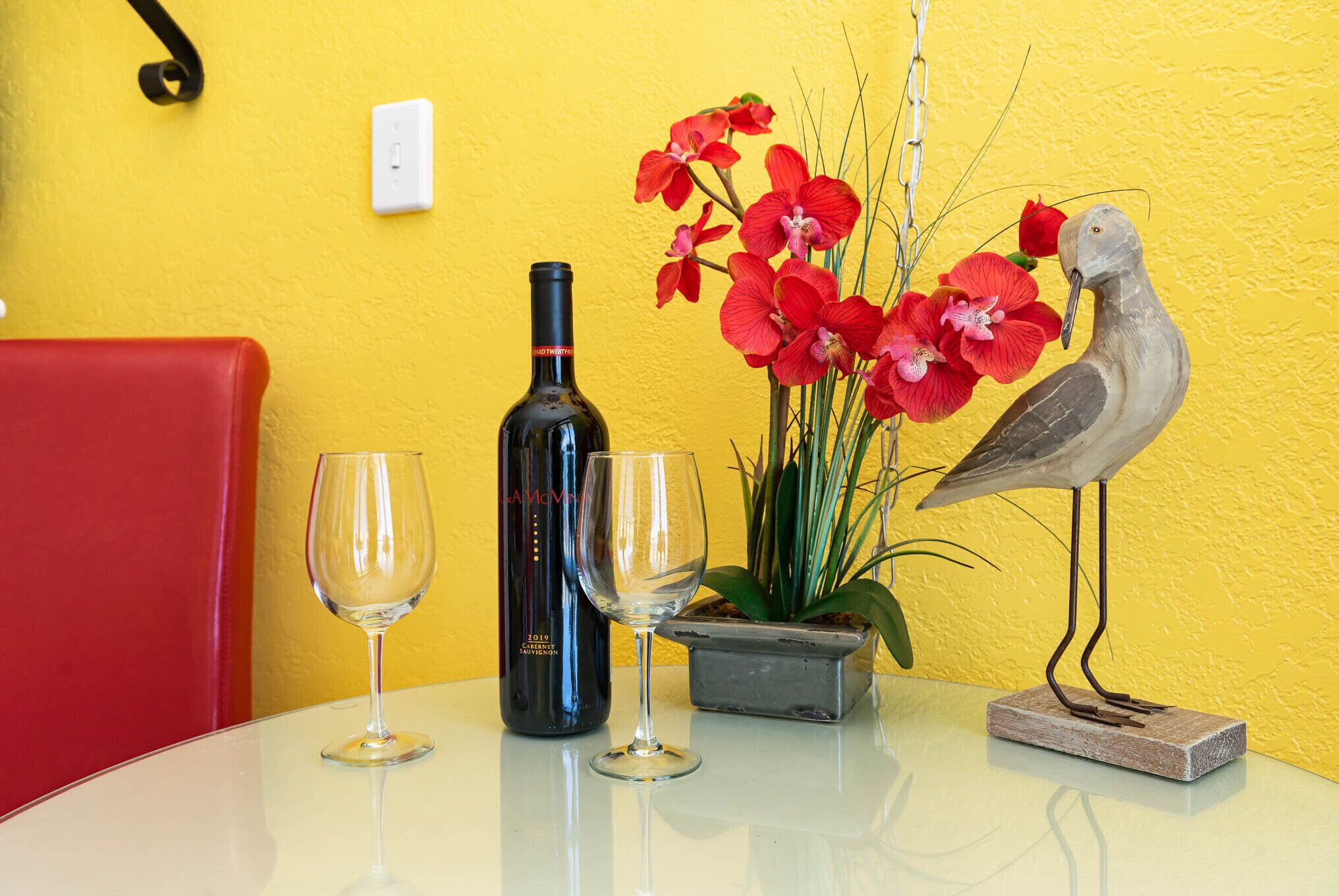 A table with a wine bottle, two glasses, a potted plant, and a bird sculpture.